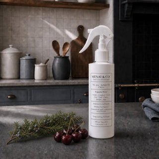 Juniper and Cherry linen and room spray styled in a kitchen with juniper branches, juniper berries, and fresh cherries.