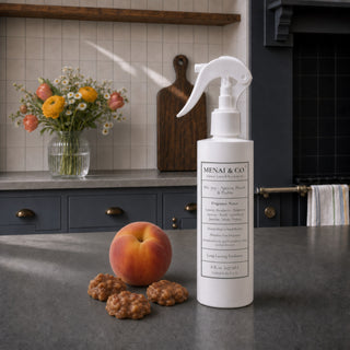 Apricot, Peach and Praline linen and room spray styled in a kitchen with a ripe peach, praline candies, and fresh flowers.