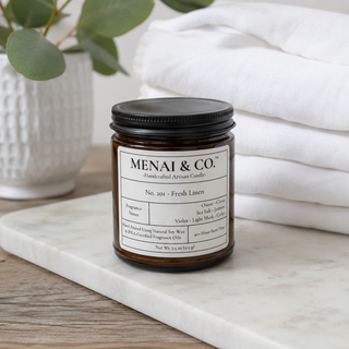 Fresh Linen soy candle in amber glass jar styled on marble tray beside folded white linens and eucalyptus stems