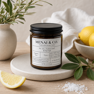 Lemon Leaf and Sea Salt soy candle in amber glass jar styled with fresh lemons, sea salt crystals, olive branches, and soft neutral linens