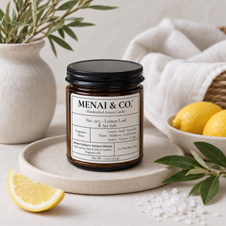 Lemon Leaf and Sea Salt soy candle in amber glass jar styled with fresh lemons, sea salt crystals, olive branches, and soft neutral linens