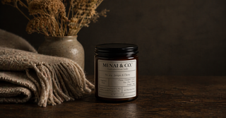 Menai & Co. amber jar candle styled on a wooden table with wool blanket in a warm, moody interior