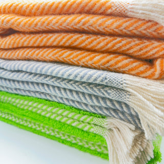 Assorted recycled wool herringbone blankets folded in a stack, featuring multiple colorways and traditional woven texture